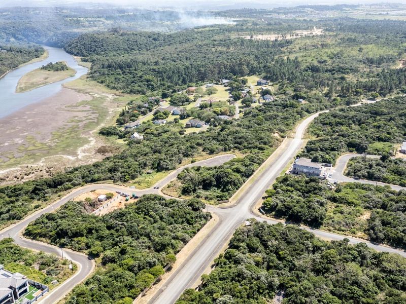 An aerial view of a residential estate featuring paved roads, established vegetation, and scenic river frontage.