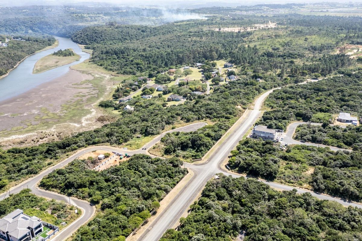 An aerial view of a residential estate featuring paved roads, established vegetation, and scenic river frontage.