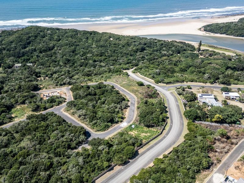 Aerial view of a residential development site featuring paved roads, surrounding natural vegetation, and proximity to the coastline and beach.