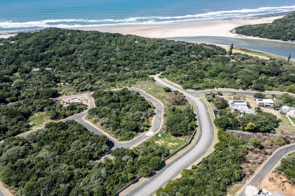 Aerial view of a residential development site featuring paved roads, surrounding natural vegetation, and proximity to the coastline and beach.