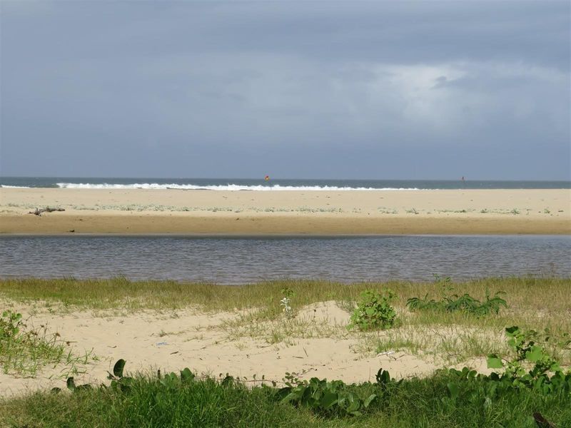 A scenic view of the coastal landscape featuring a sandy beach, a calm water body, and the ocean horizon.