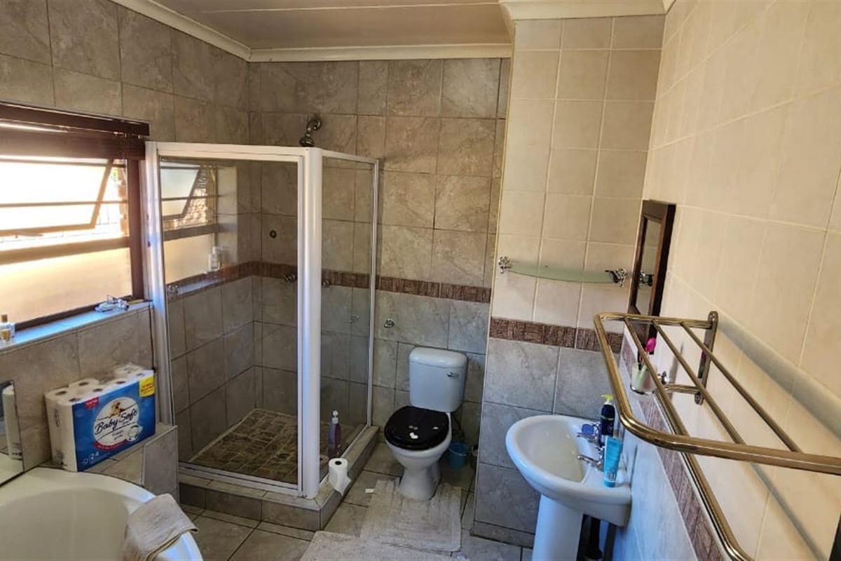 A functional bathroom featuring a corner bathtub, a separate glass-enclosed shower, a pedestal basin, and a toilet, finished with neutral wall and floor tiling.