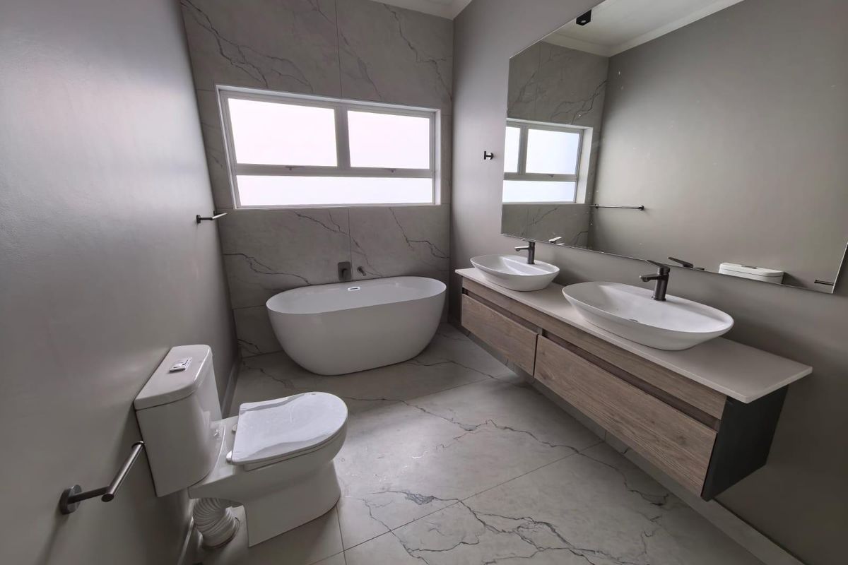 Modern bathroom featuring a freestanding bathtub, double vanity with vessel sinks, large wall-mounted mirror, and marble-look floor and wall tiling.