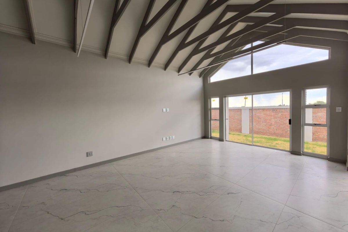 Spacious living area featuring high vaulted ceilings with exposed beams, large windows, and modern marble-look floor tiles, offering a bright and open atmosphere.