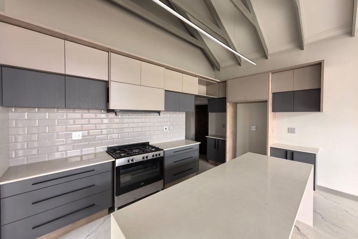 Modern kitchen featuring two-tone cabinetry, stone countertops, a central island, gas stove with extractor fan, and high vaulted ceilings with exposed beams.