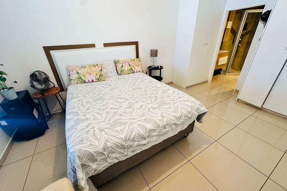 A well-maintained bedroom featuring large format floor tiles, built-in cupboards, and an en-suite bathroom access.