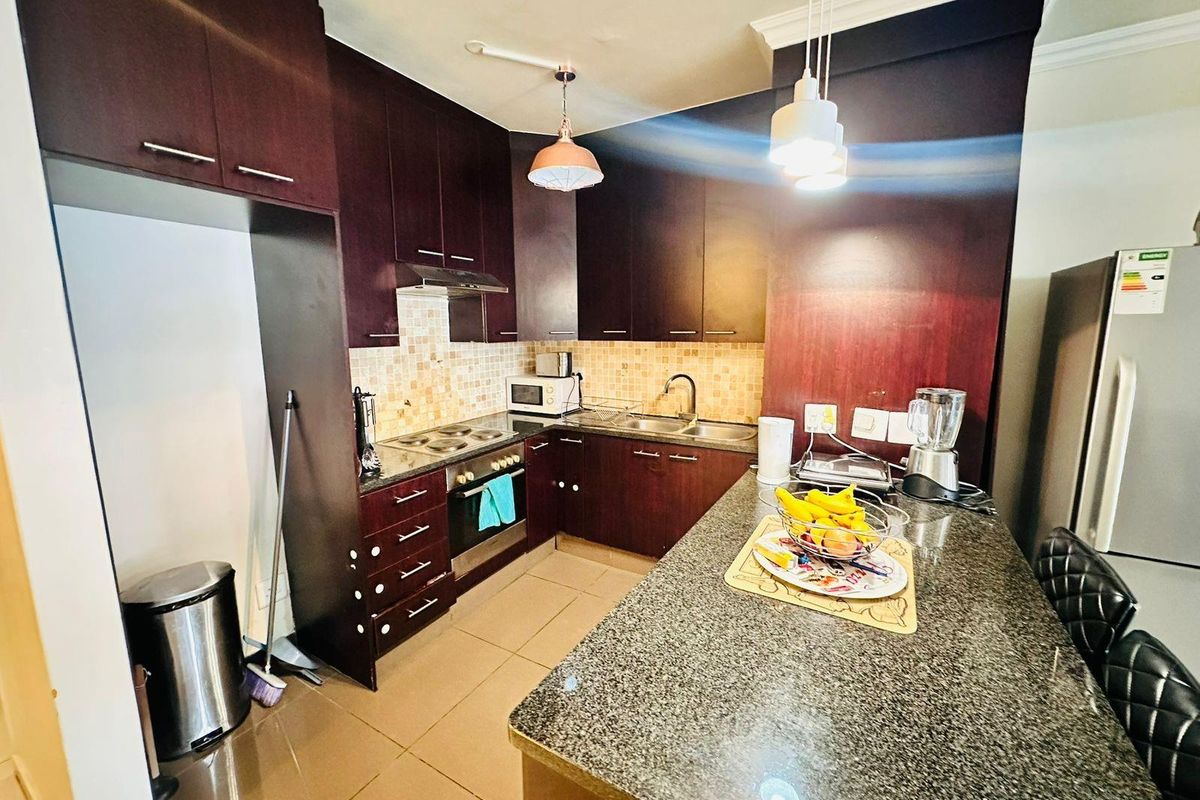A functional kitchen featuring dark wood cabinetry, granite countertops, a breakfast bar, tiled backsplash, and built-in oven with extractor fan.