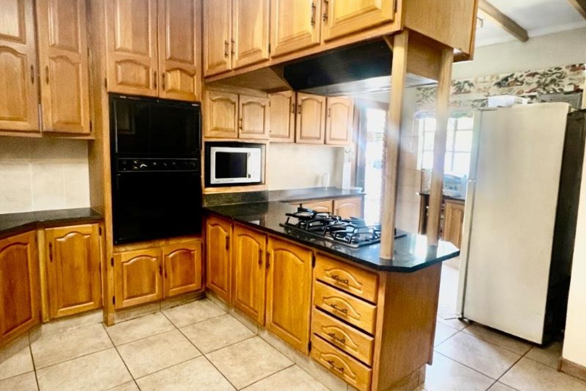A functional kitchen featuring traditional timber cabinetry, dark stone countertops, a built-in oven, and a gas hob with an integrated extractor fan.