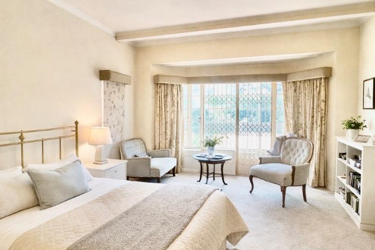 Spacious bedroom featuring a large bay window with security gate, neutral carpeting, and a modern ceiling fan.