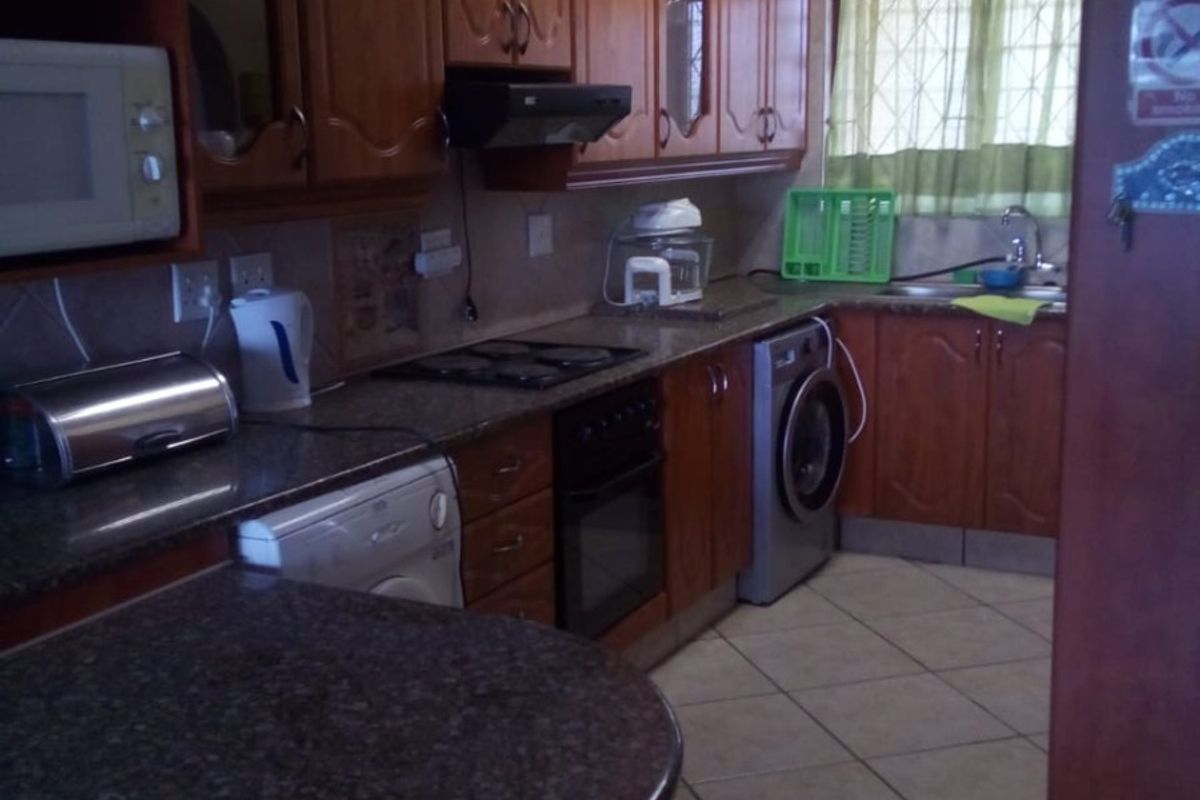 A functional kitchen featuring wooden cabinetry, granite countertops, built-in oven, hob, and tiled flooring, offering a practical layout for daily use.