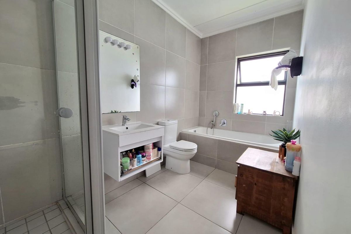 A modern bathroom featuring a glass-enclosed shower, a built-in bathtub, a wall-mounted vanity with a basin, and neutral floor-to-ceiling tiling.