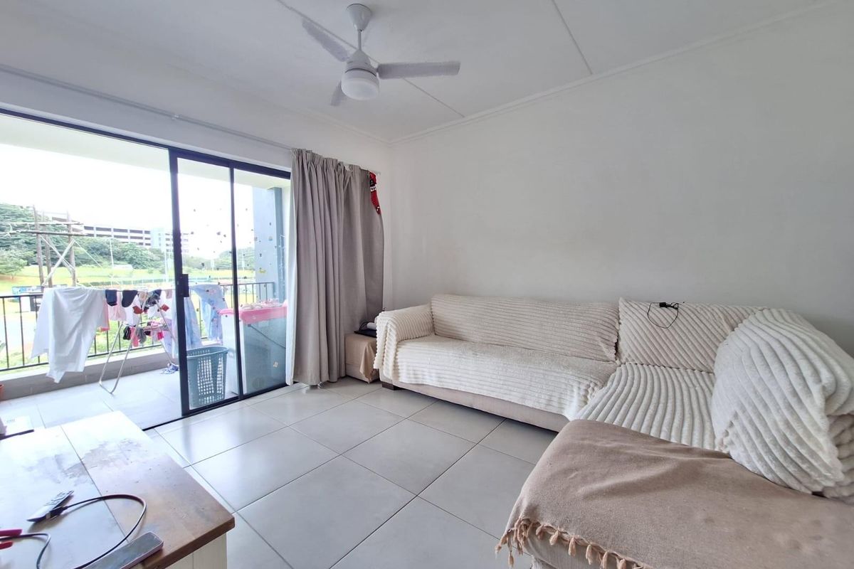 A bright living room featuring large sliding glass doors that open onto a private balcony, complete with tiled flooring and a ceiling fan.