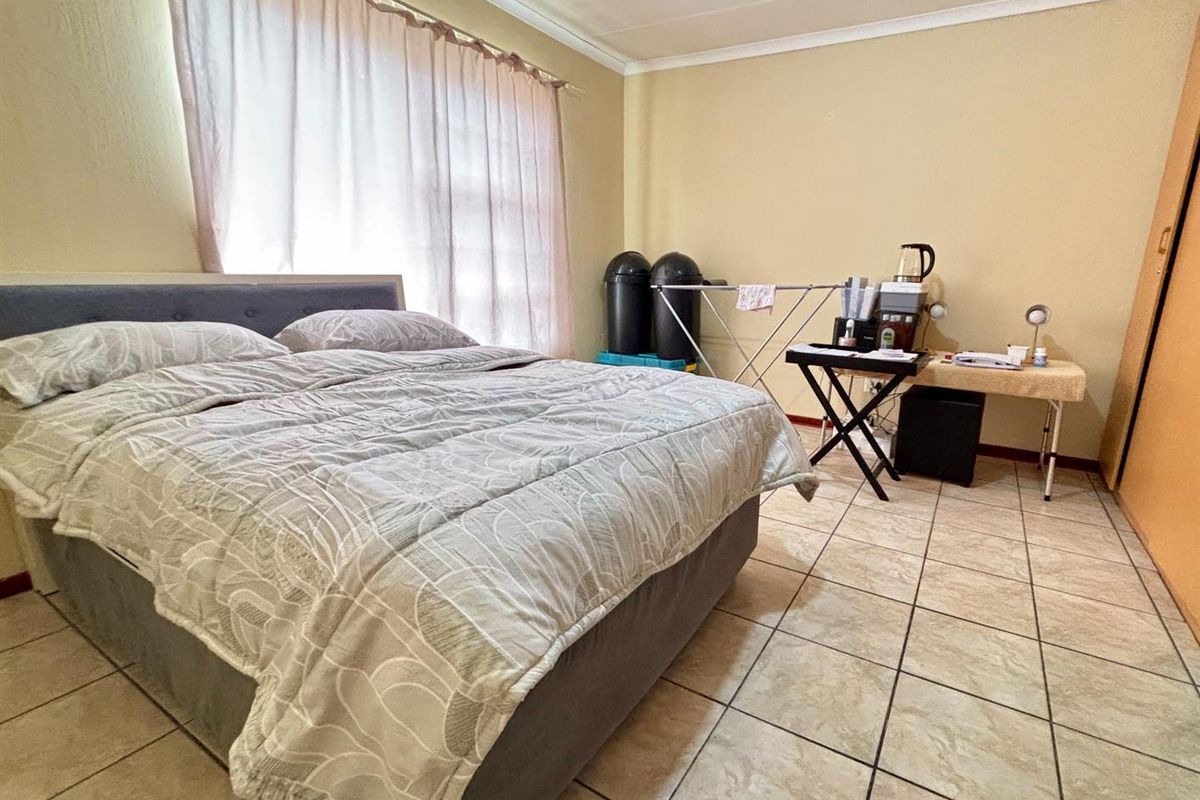 A functional bedroom featuring tiled flooring, built-in cupboard space, and large windows allowing for natural light.