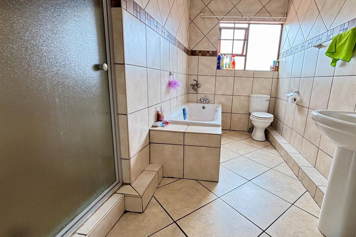 A functional bathroom featuring a tiled shower enclosure, a built-in bathtub, a pedestal sink, and a toilet with neutral wall and floor tiling.
