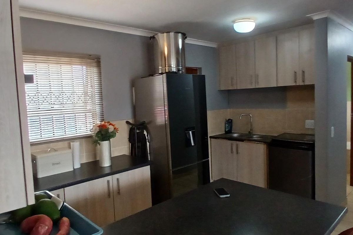 A functional kitchen featuring light wood cabinetry, dark countertops, a stainless steel sink, and a built-in extractor fan.