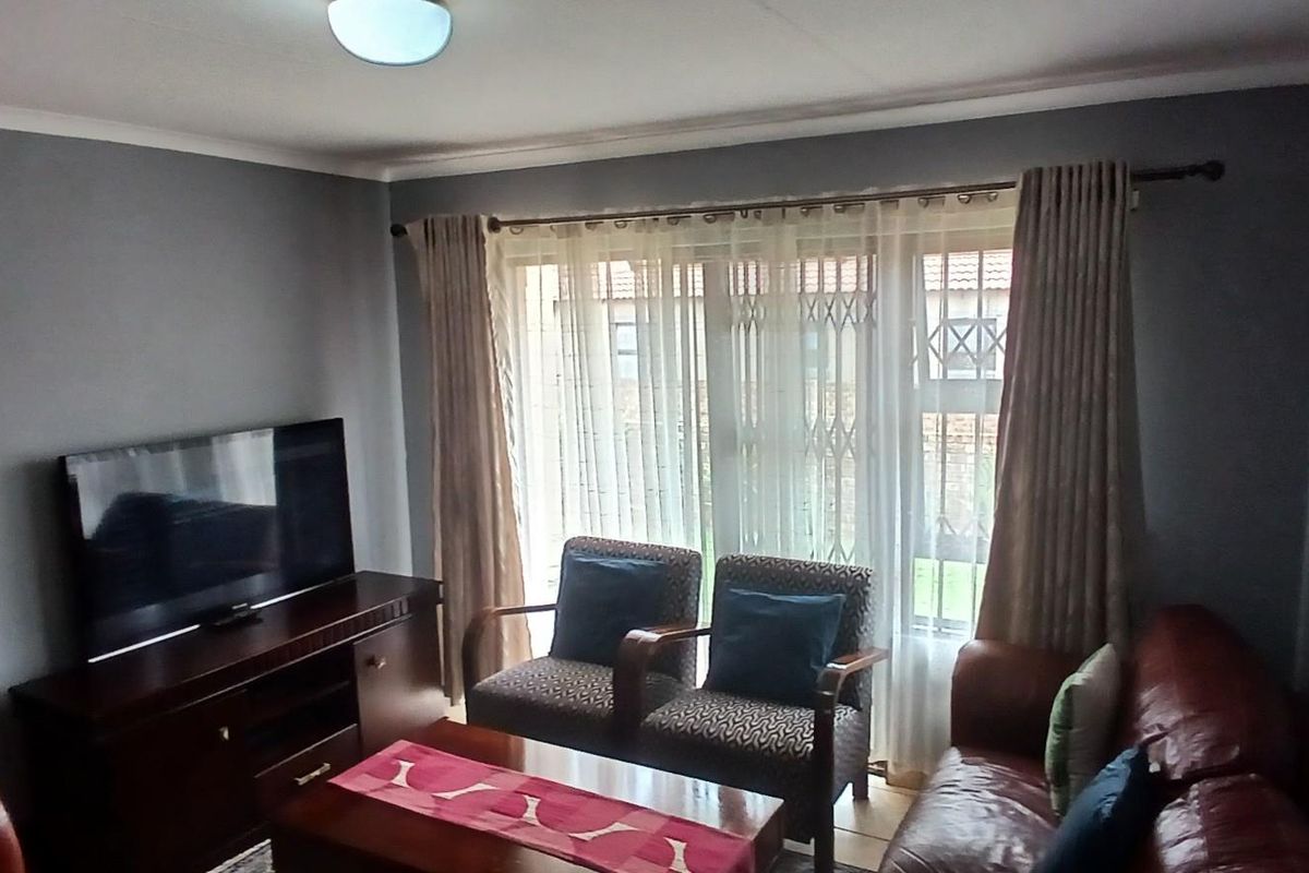 A comfortable living room featuring grey walls, crown molding, and a large window with security gate access to the exterior.
