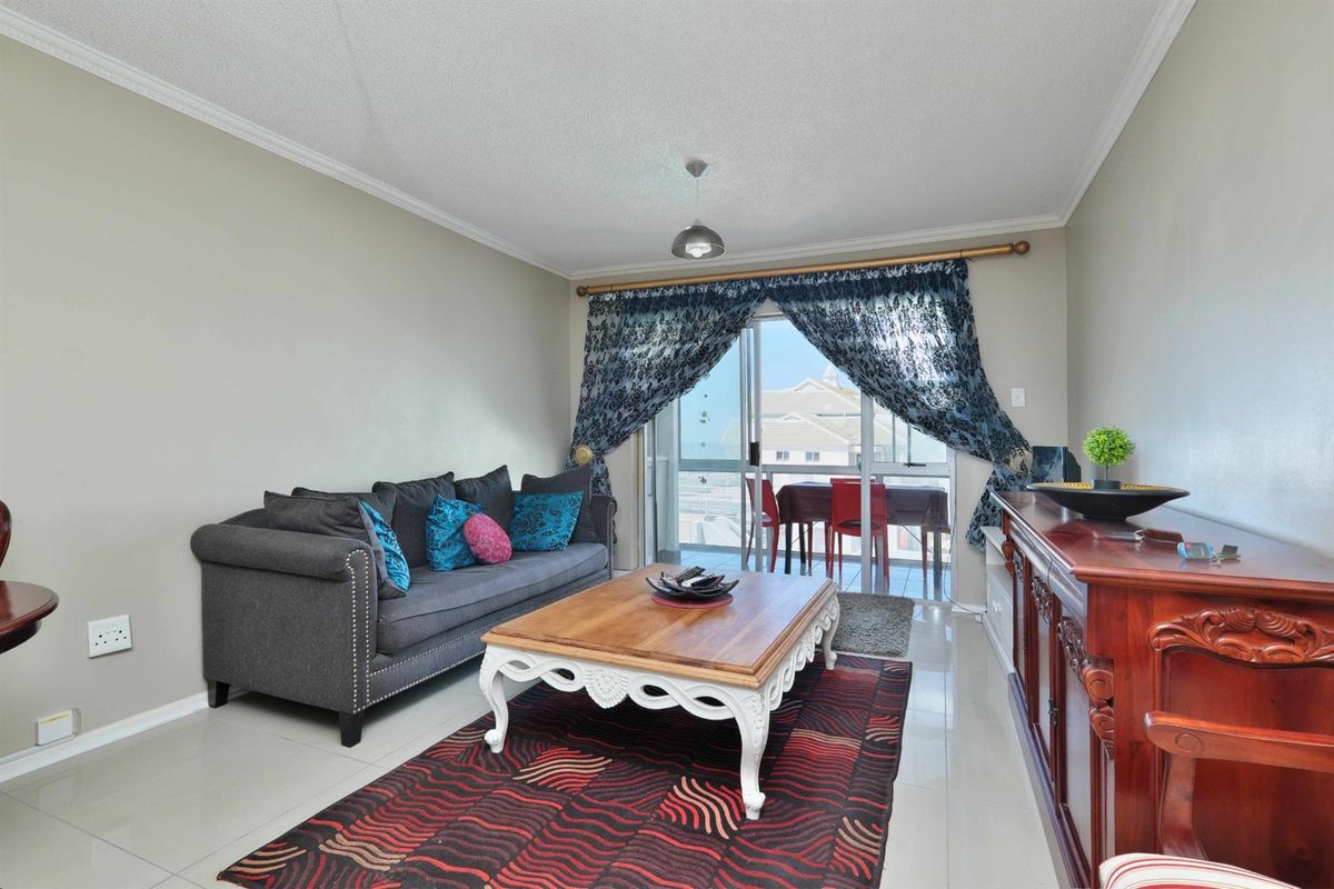 A bright living room featuring tiled flooring, crown molding, and sliding glass doors that open onto a balcony with exterior views.