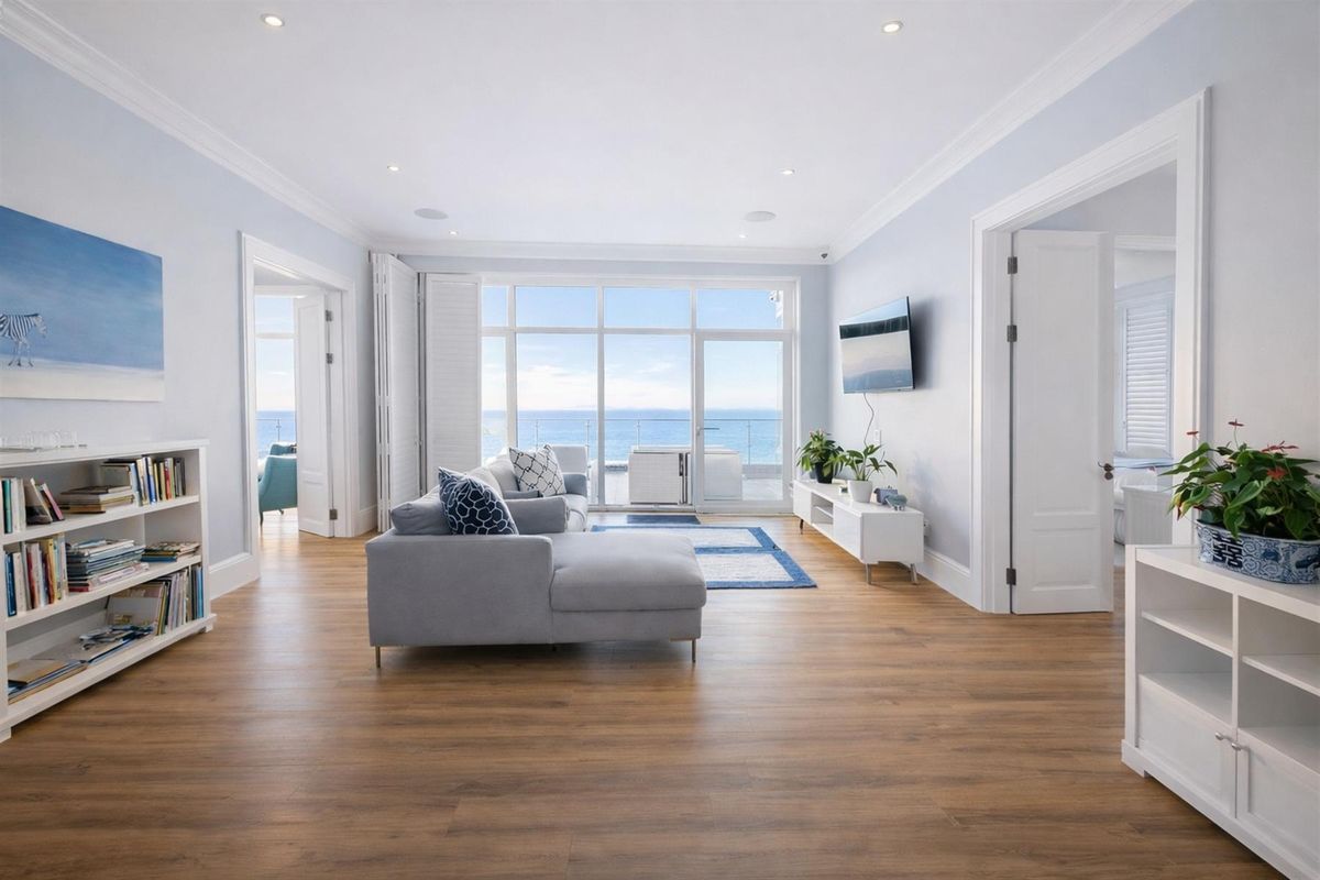 Bright and spacious living room featuring timber flooring, crown molding, recessed lighting, and expansive glass doors offering panoramic ocean views.