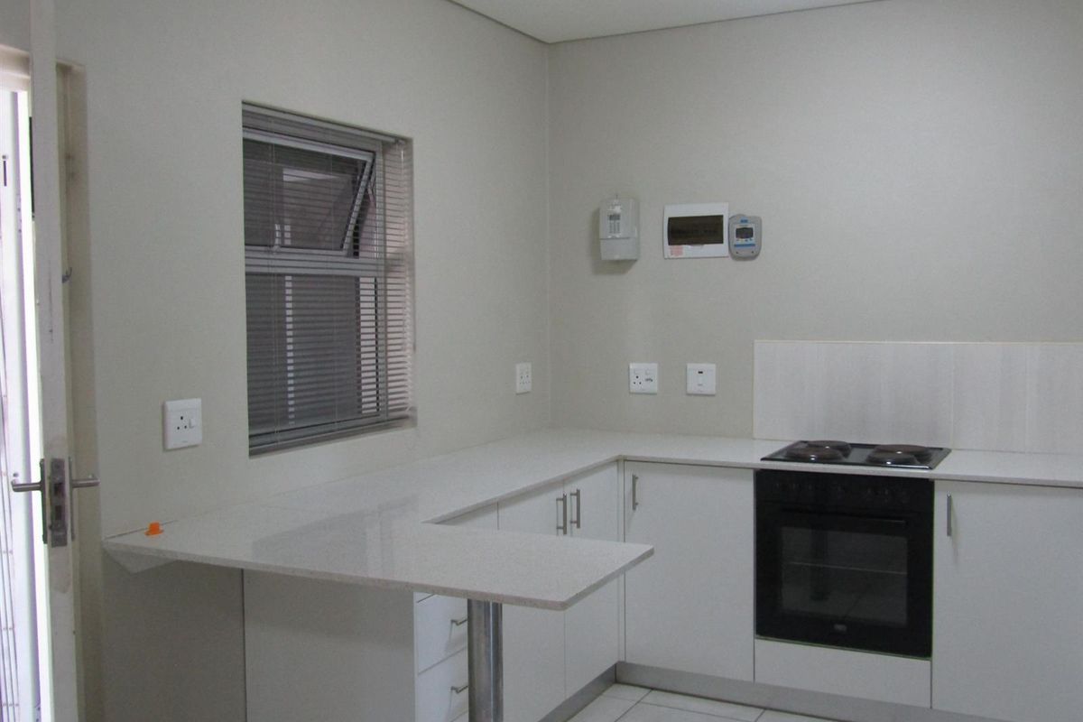 A clean, modern kitchen featuring white cabinetry, stone countertops, a breakfast bar, and a built-in electric oven and hob.