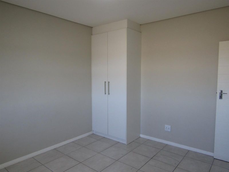A clean, empty bedroom featuring neutral wall paint, tiled flooring, and a built-in white wardrobe.