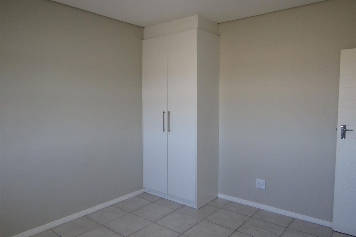 A clean, empty bedroom featuring neutral wall paint, tiled flooring, and a built-in white wardrobe.