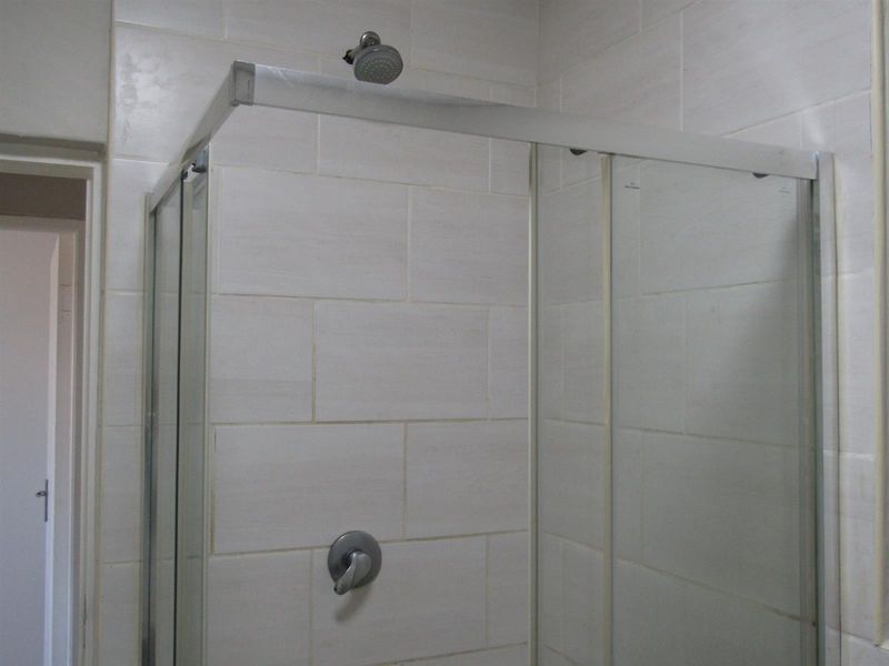 A functional bathroom shower area featuring a glass enclosure, wall tiling, and a standard shower mixer tap.