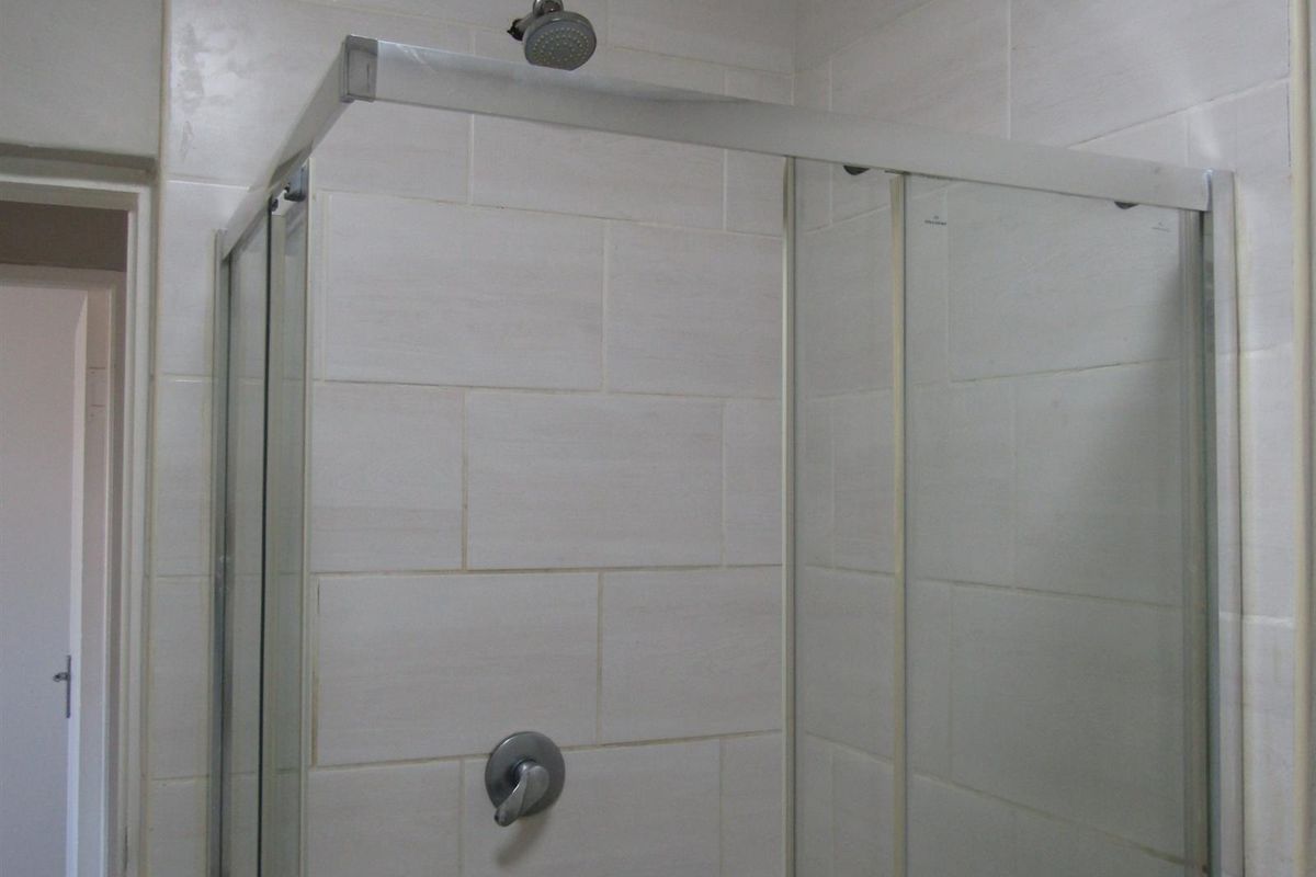 A functional bathroom shower area featuring a glass enclosure, wall tiling, and a standard shower mixer tap.