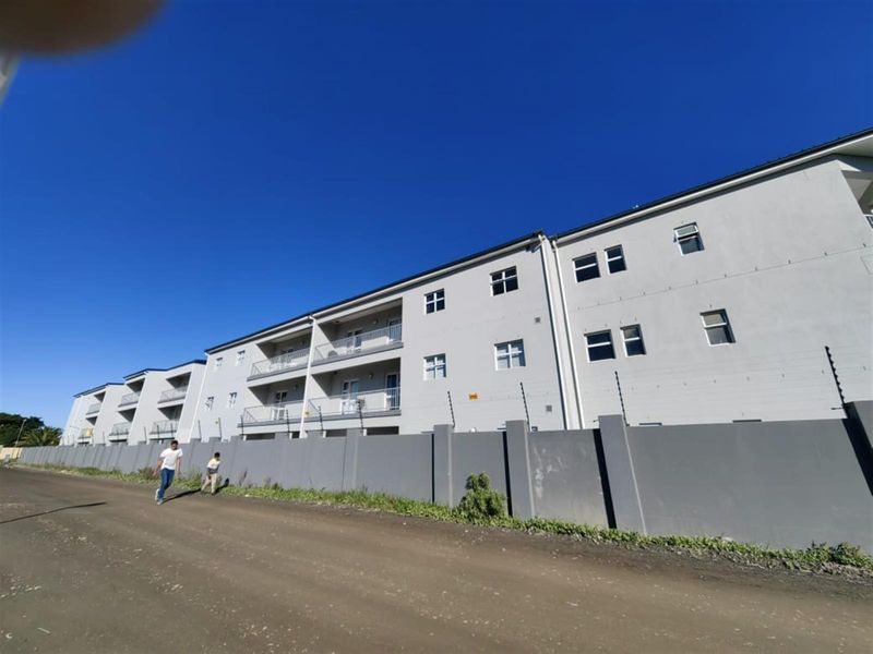 Exterior view of a multi-story apartment complex featuring a perimeter wall with electric fencing and private balconies for each unit.