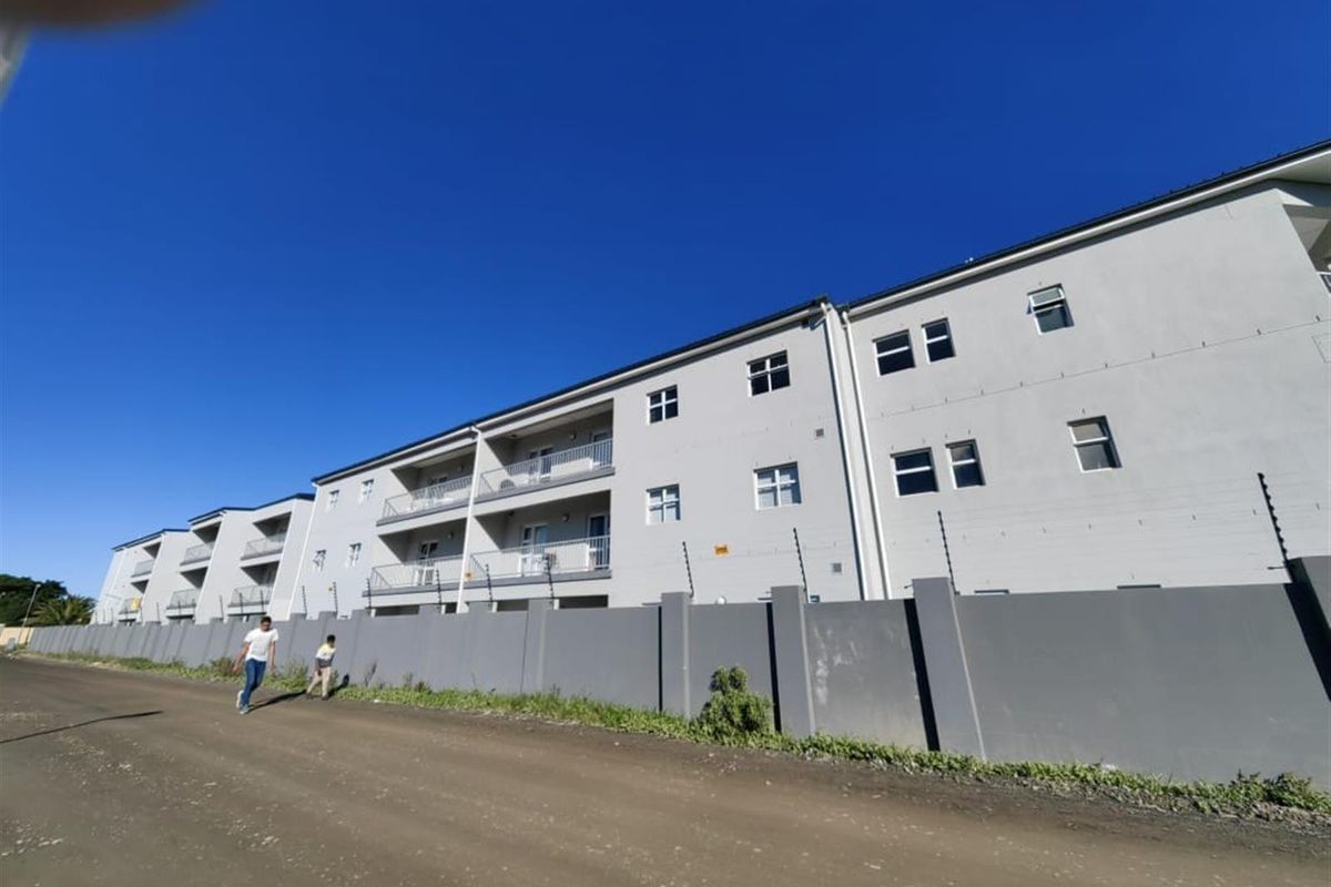 Exterior view of a multi-story apartment complex featuring a perimeter wall with electric fencing and private balconies for each unit.