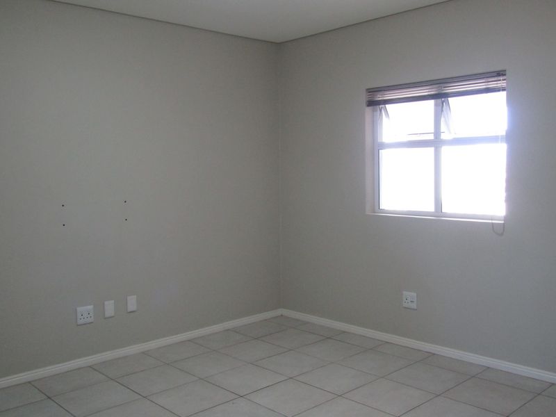 An empty bedroom featuring neutral tiled flooring, light-colored walls, and a window with fitted blinds, ready for personalization.