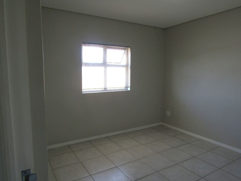 An empty bedroom featuring neutral wall paint, tiled flooring, and a window with fitted blinds.