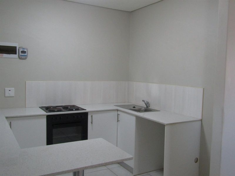 A clean, functional kitchen featuring white cabinetry, a built-in oven with electric hob, stainless steel sink, and neutral tiled splashback.
