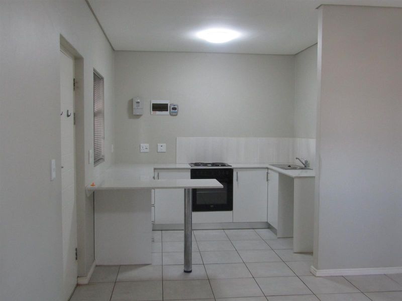 A clean, modern kitchen featuring white cabinetry, a built-in oven and hob, tiled flooring, and a functional breakfast counter.