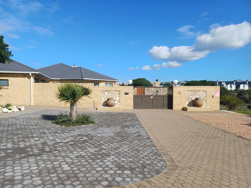 Front exterior view of the property featuring a paved driveway, brick boundary wall with stone accents, and a secure metal entrance gate.