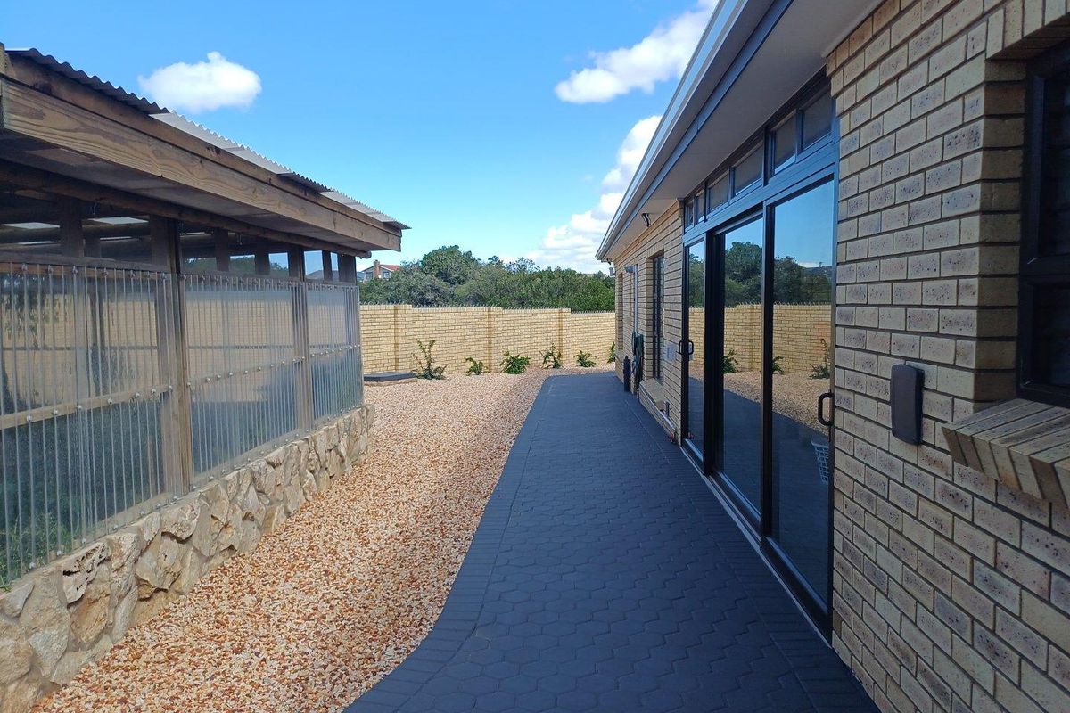 A well-maintained side exterior area featuring a paved walkway, brick facade, and a secondary structure with stone base and corrugated roofing.