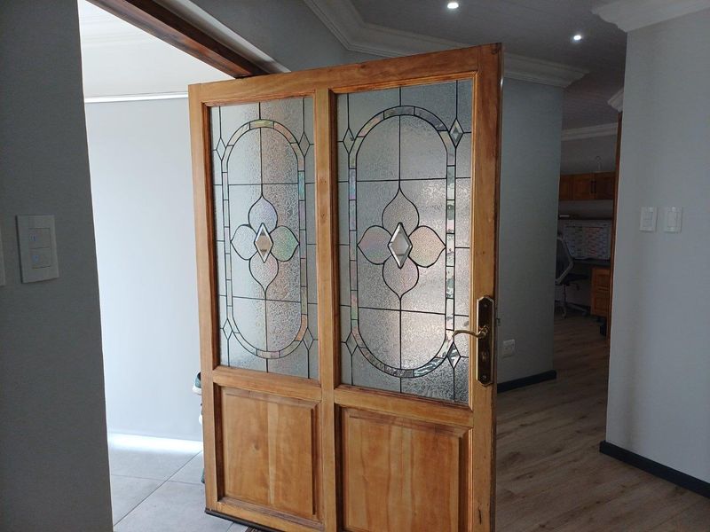 A solid timber double door featuring decorative leaded glass panels, serving as an elegant interior transition between living spaces.