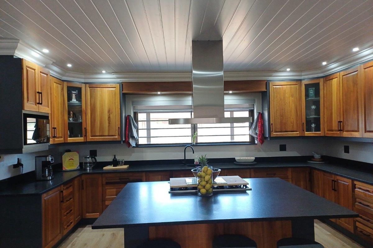 A well-appointed kitchen featuring wooden cabinetry, dark stone countertops, a central island with a built-in hob, and a stainless steel extractor fan.