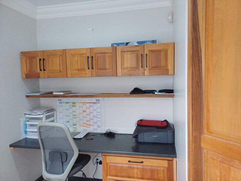 A dedicated home office space featuring built-in wooden cabinetry, overhead storage cupboards, and a laminate desk surface.