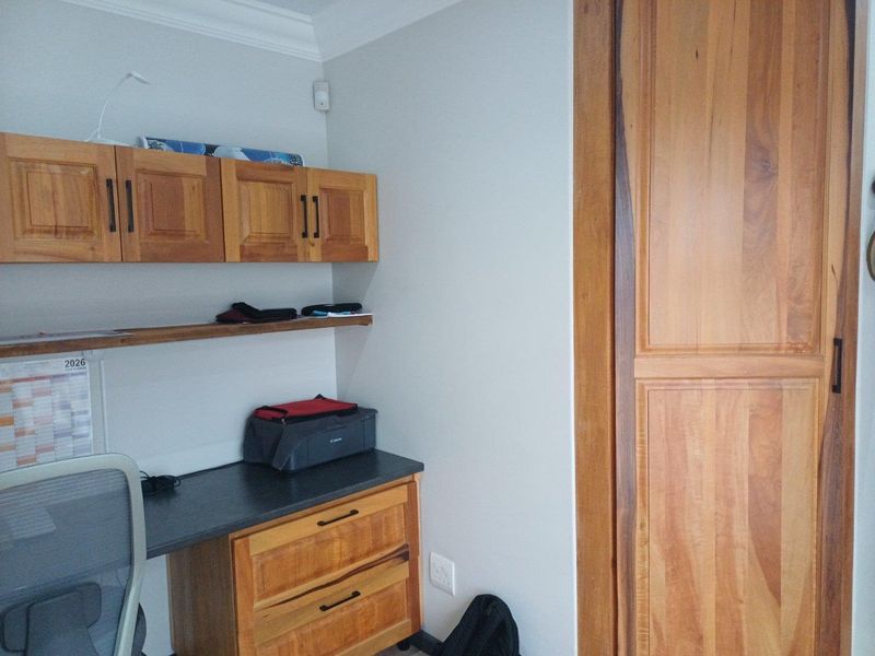 A functional home office space featuring built-in wooden cabinetry, a desk workstation, and a solid wood door.