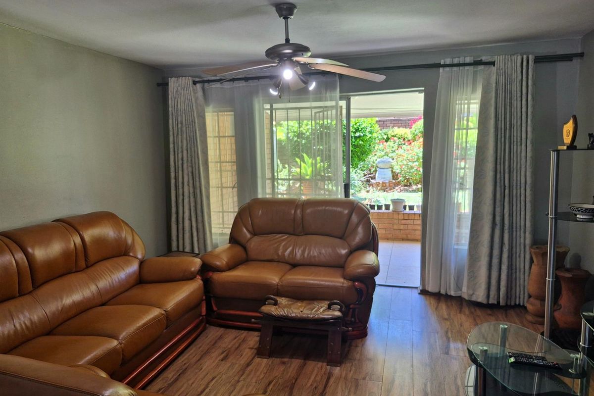 A comfortable living room featuring wood-look flooring, a ceiling fan, and large sliding glass doors that open onto a private patio and garden area.