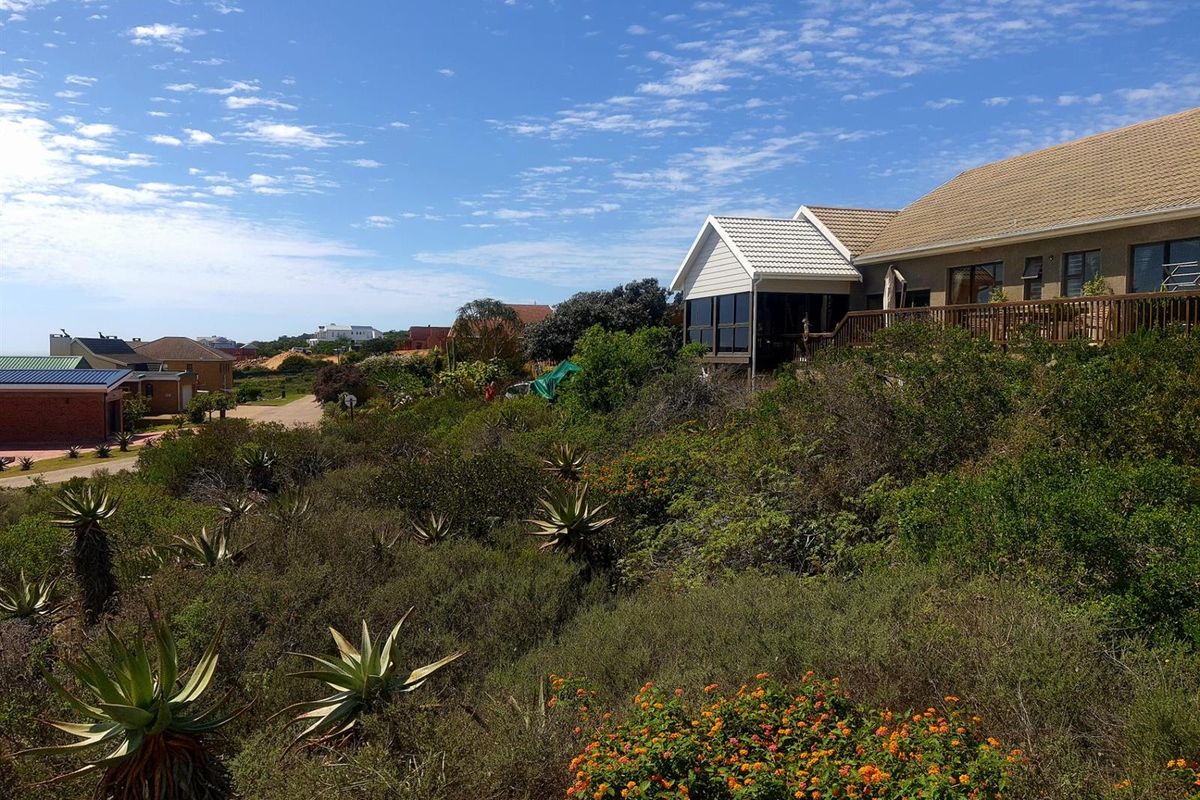 A view of the rear elevation of a residential property featuring a wooden deck, tiled roof, and established garden with native vegetation.