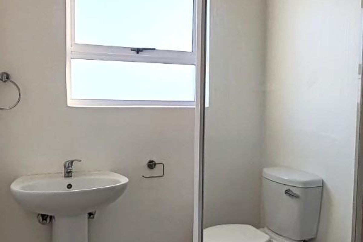 A functional bathroom featuring a pedestal basin, a standard toilet, and a glass-enclosed shower with tiled flooring.