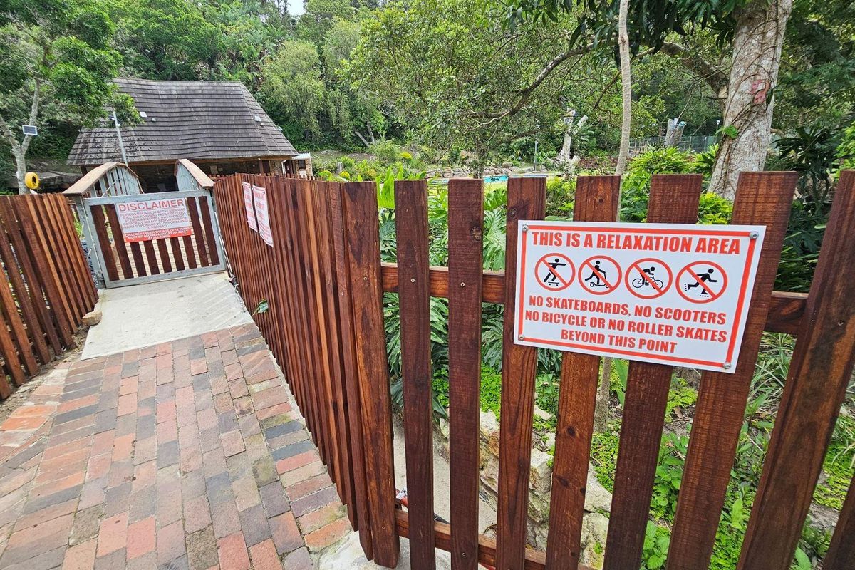 A paved walkway leading to a gated entrance of a communal relaxation area, featuring timber fencing and signage.