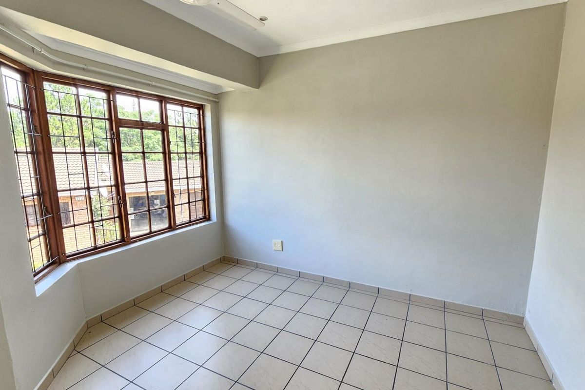 A bright, empty bedroom featuring tiled flooring and large wooden-framed windows with security bars, offering a clean and neutral space ready for personalization.