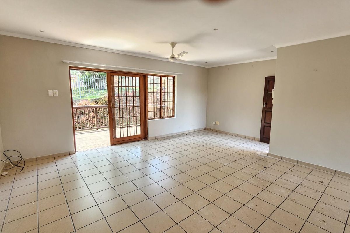 Spacious open-plan living area featuring tiled flooring, a ceiling fan, and sliding glass doors providing direct access to an outdoor patio.