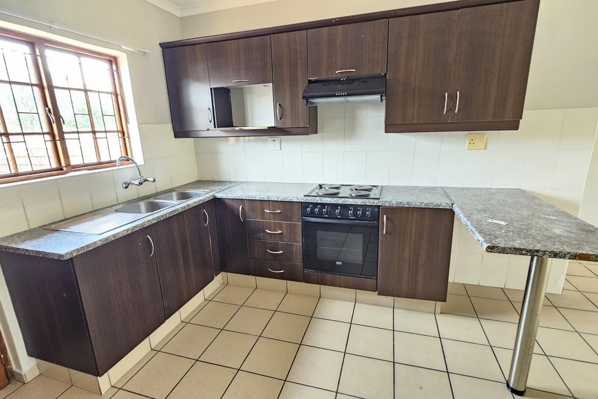 Functional kitchen featuring dark wood cabinetry, granite-look countertops, a built-in oven with hob, extractor fan, and a double stainless steel sink.