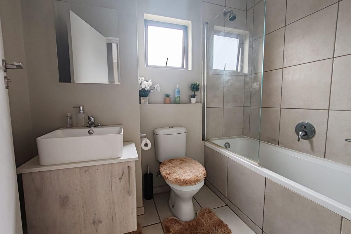 A functional bathroom featuring a modern vessel sink vanity, a combined bathtub and shower with glass screen, and neutral wall tiling.