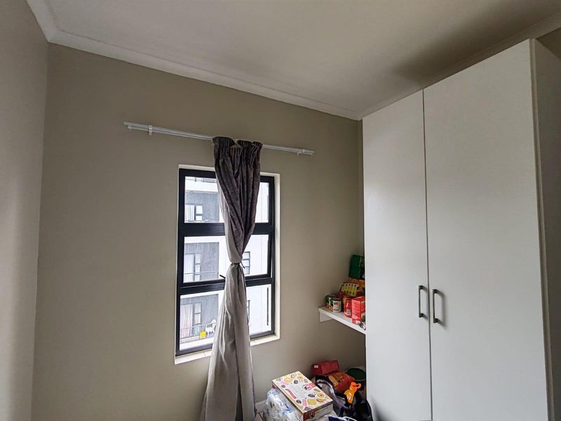 A bedroom featuring a built-in white wardrobe and a window with a curtain rod.