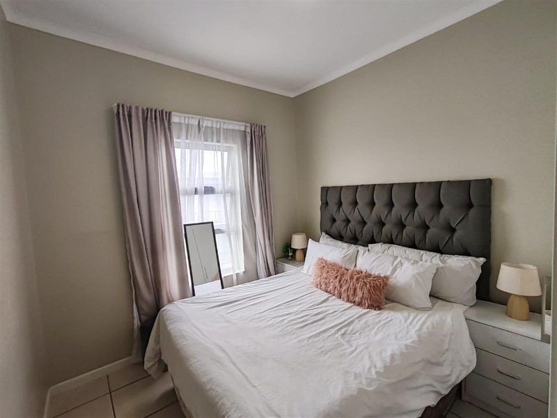 A well-maintained bedroom featuring neutral wall tones, tiled flooring, and a large window with curtain treatments.