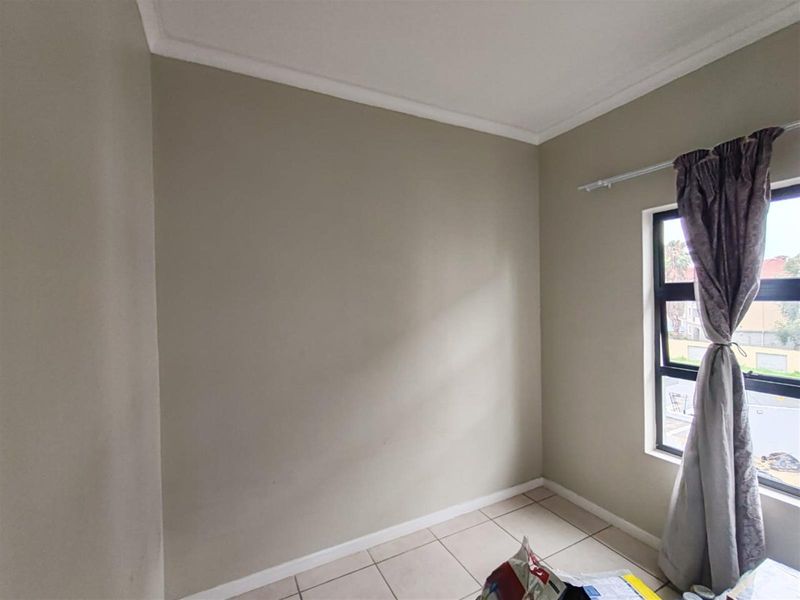 A simple bedroom featuring neutral wall paint, tiled flooring, and a window with curtain rod.
